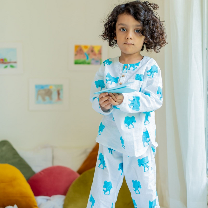 Dumbo Night Suit Set A child standing in a room wearing a long-sleeved white night suit with blue elephant prints, featuring a round neckline and full sleeves.