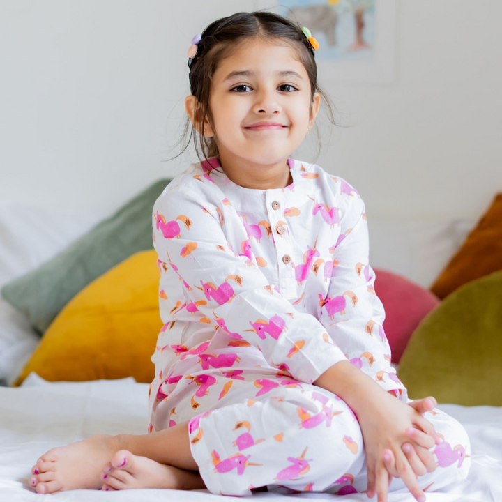 Pinkie Pie Girls Night Suit Set A girl sitting on a bed, wearing a pink character-themed night suit set with pockets.