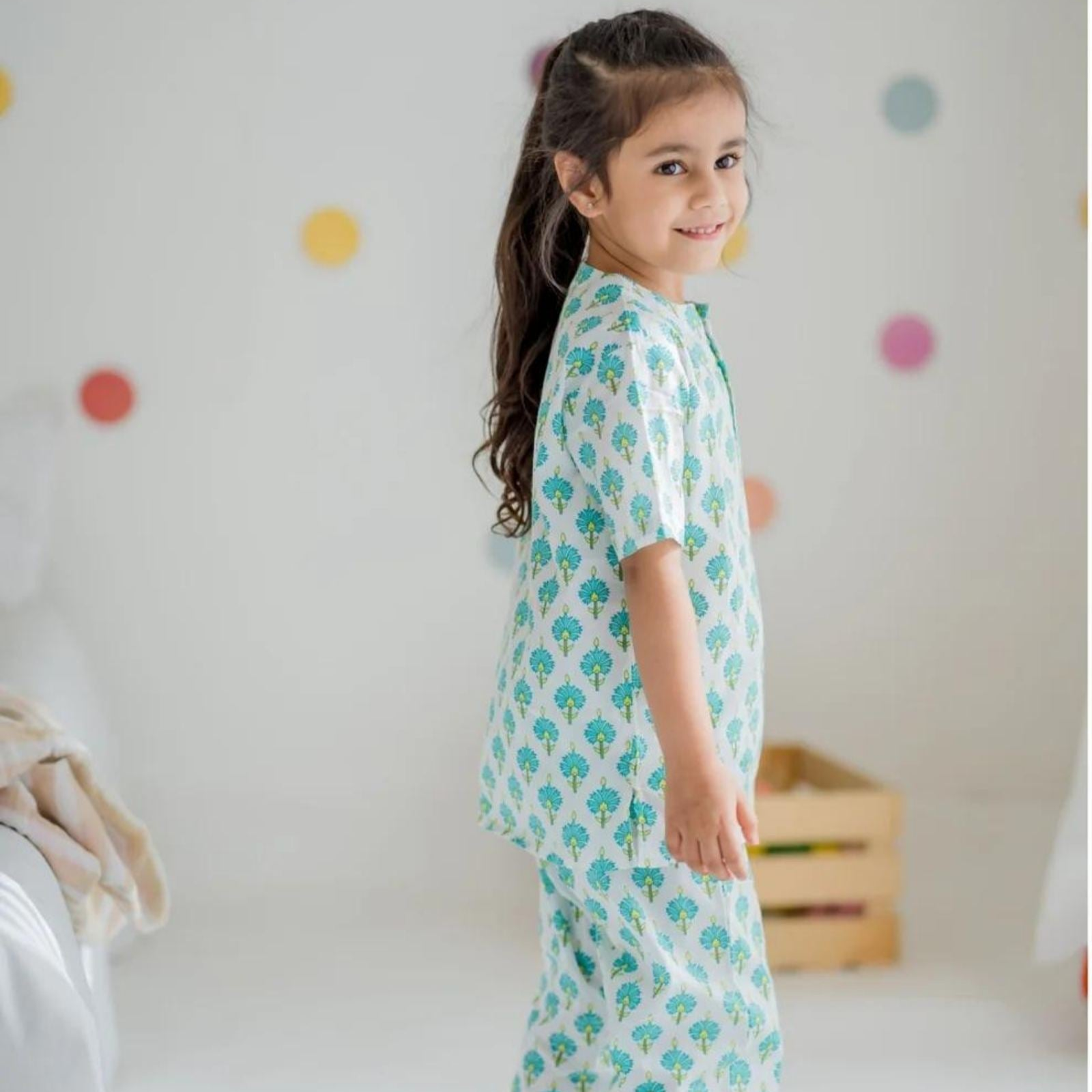 Bluebell Girls Night Suit Set A girl wearing a long sleeve night suit with half-length pants, both with a similar pattern, standing in a room with colorful dots on the wall.