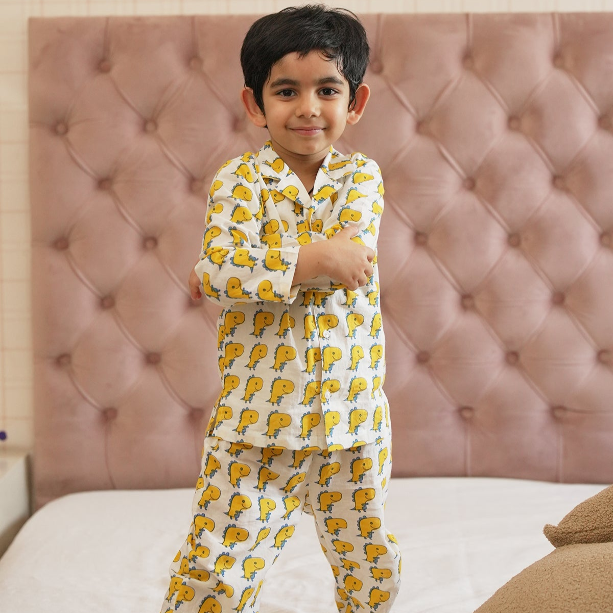 Dino Print Night Suit Set A child standing in a bedroom wearing a long sleeve night suit with dinosaur print.
