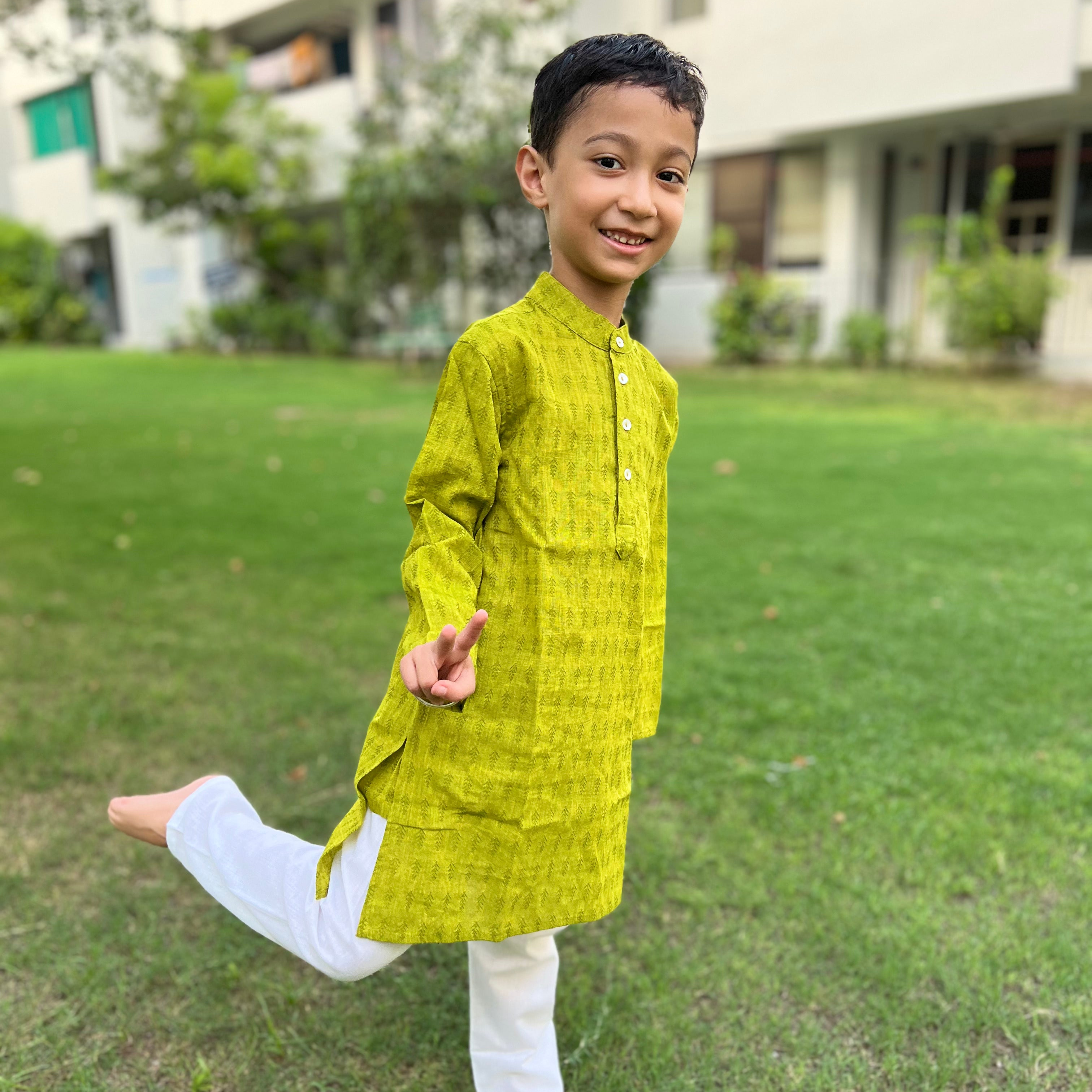Green Cotton Dobby Kurta A child wearing a green cotton dobby long kurta with full sleeves and a Chinese collar, standing on grass.