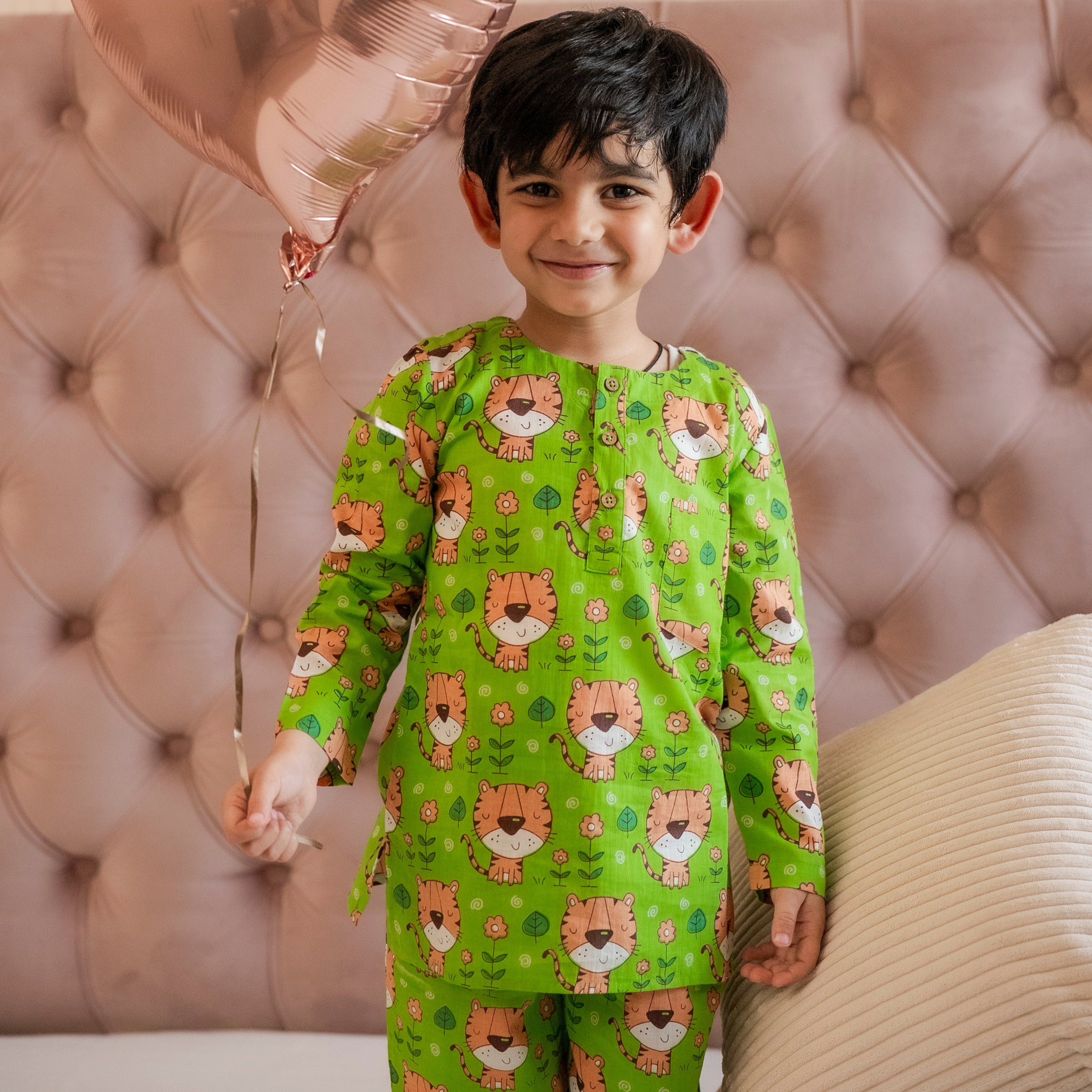 Green Tiger Night Suit Set Loungewear A child standing and smiling, wearing a green night suit set with a pattern of cartoonish animals, holding a pink balloon.
