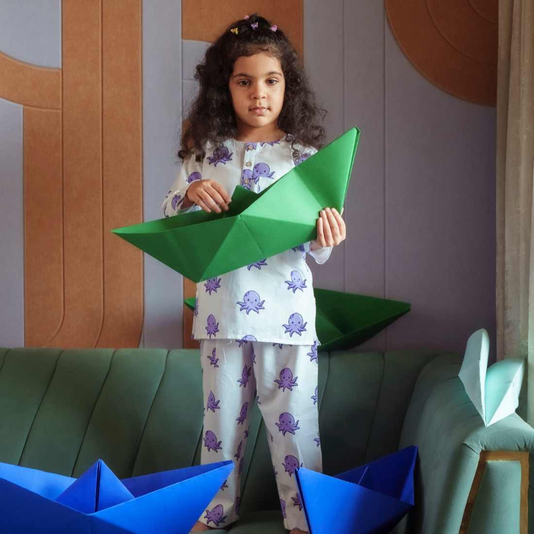 Octopus Print PJ set Sleepwear A child standing on a sofa, holding a green paper boat, wearing a white long-sleeved PJ set with an octopus print.