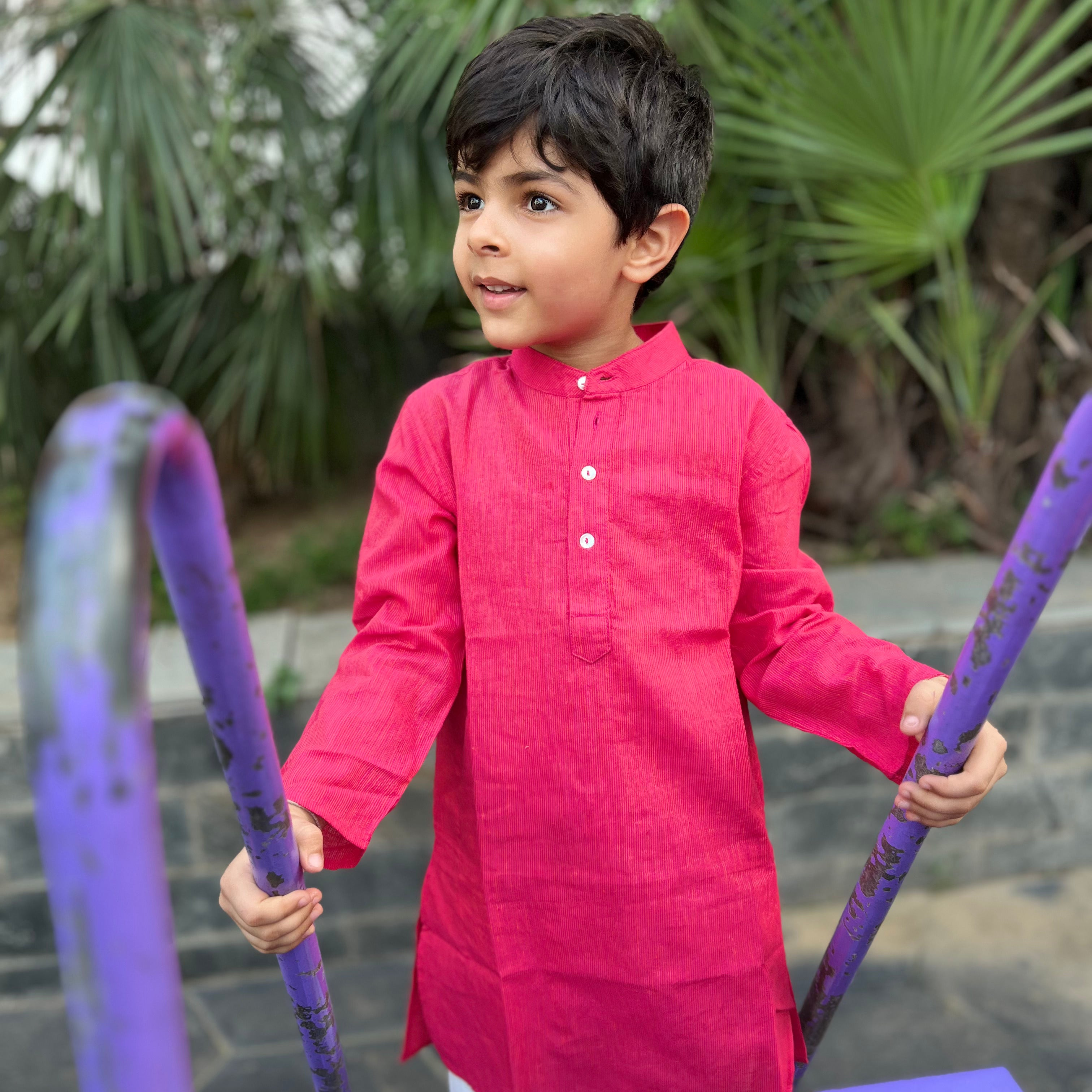 Pink Cotton Dobby Kurta A child in a pink kurta with full sleeves and a Chinese collar, standing next to a purple dabka with dobby pattern.