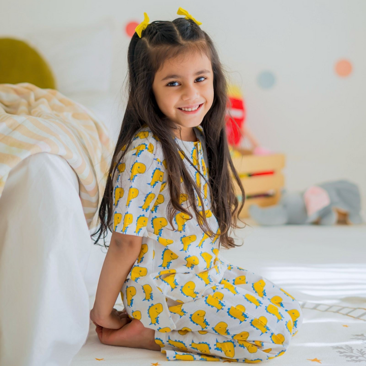 Rex Night Suit Set A child sitting on the floor wearing a yellow and white night suit with animal print and pockets on the front.