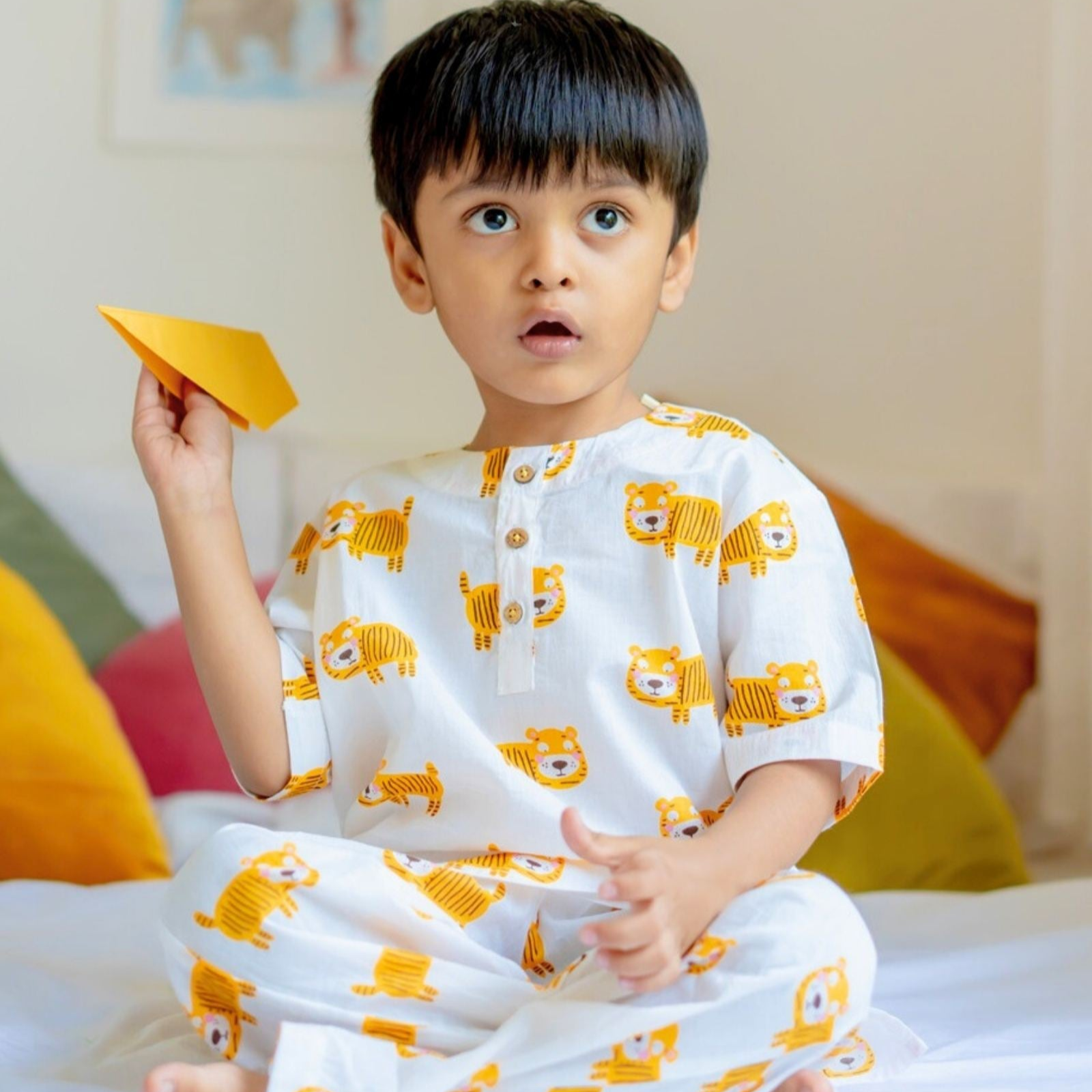 Tigger Night Suit Set A child sitting on a bed wearing a white and orange Tigger night suit set, holding a orange toy car.